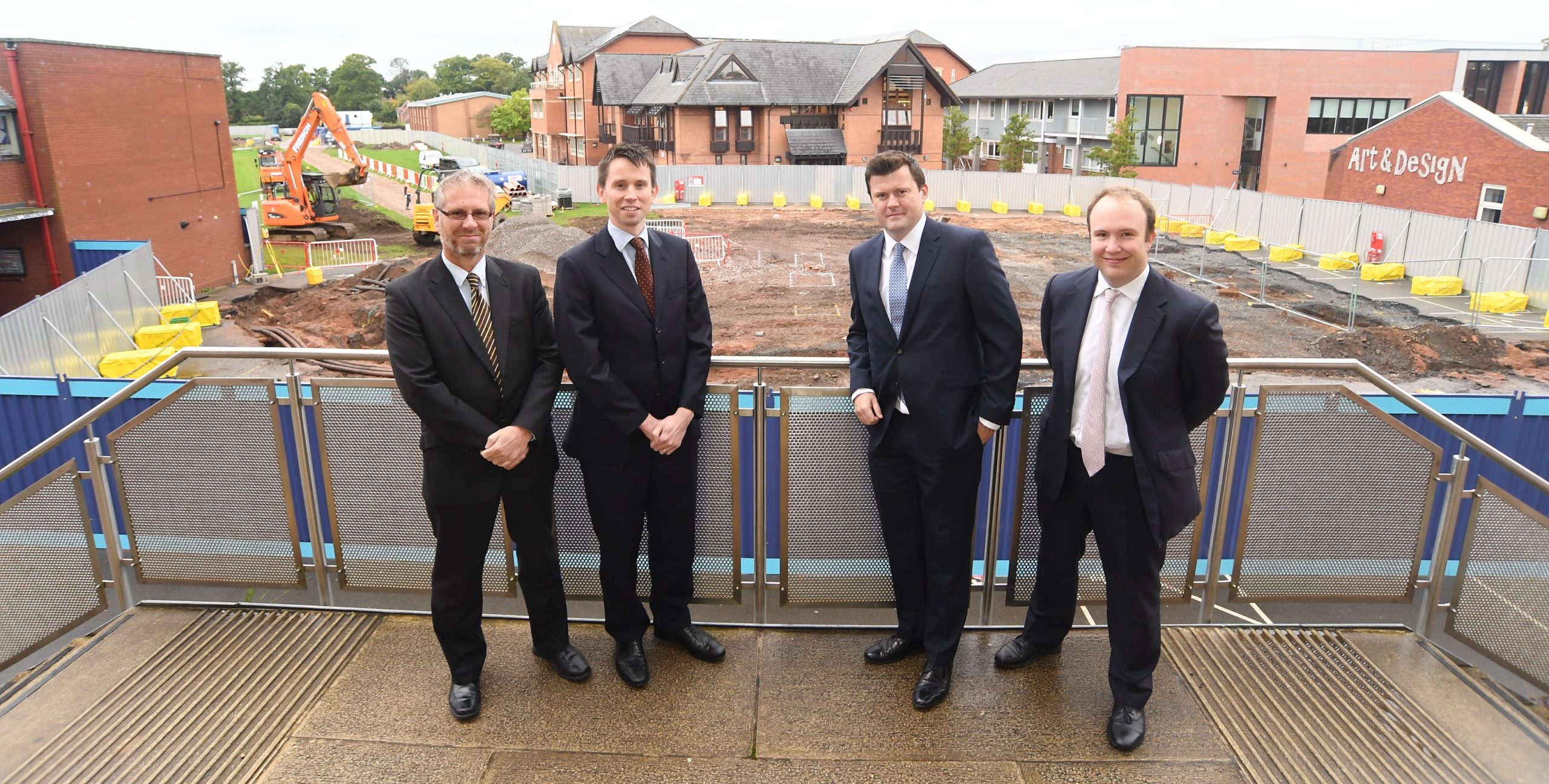 Four attorneys standing on a balcony overlooking a construction site with machinery and safety barriers.