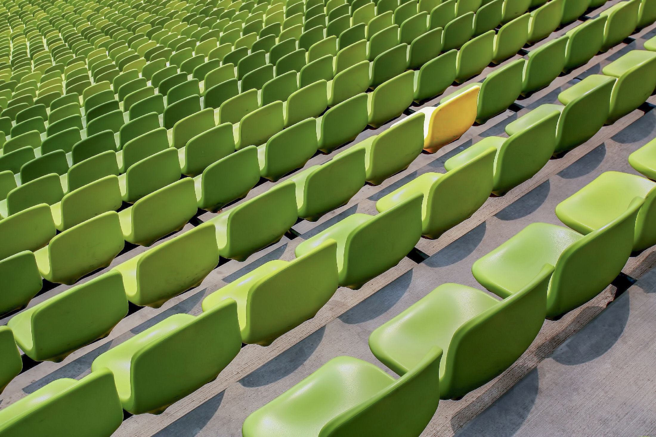 Rows of green stadium seats with one yellow seat visible among them.