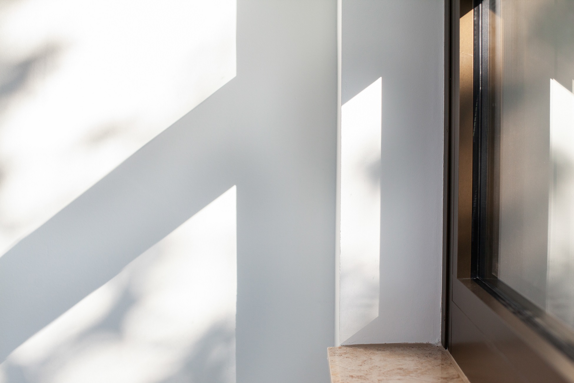 Bright interior corner with window, shadows creating geometric patterns on the walls and ledge.