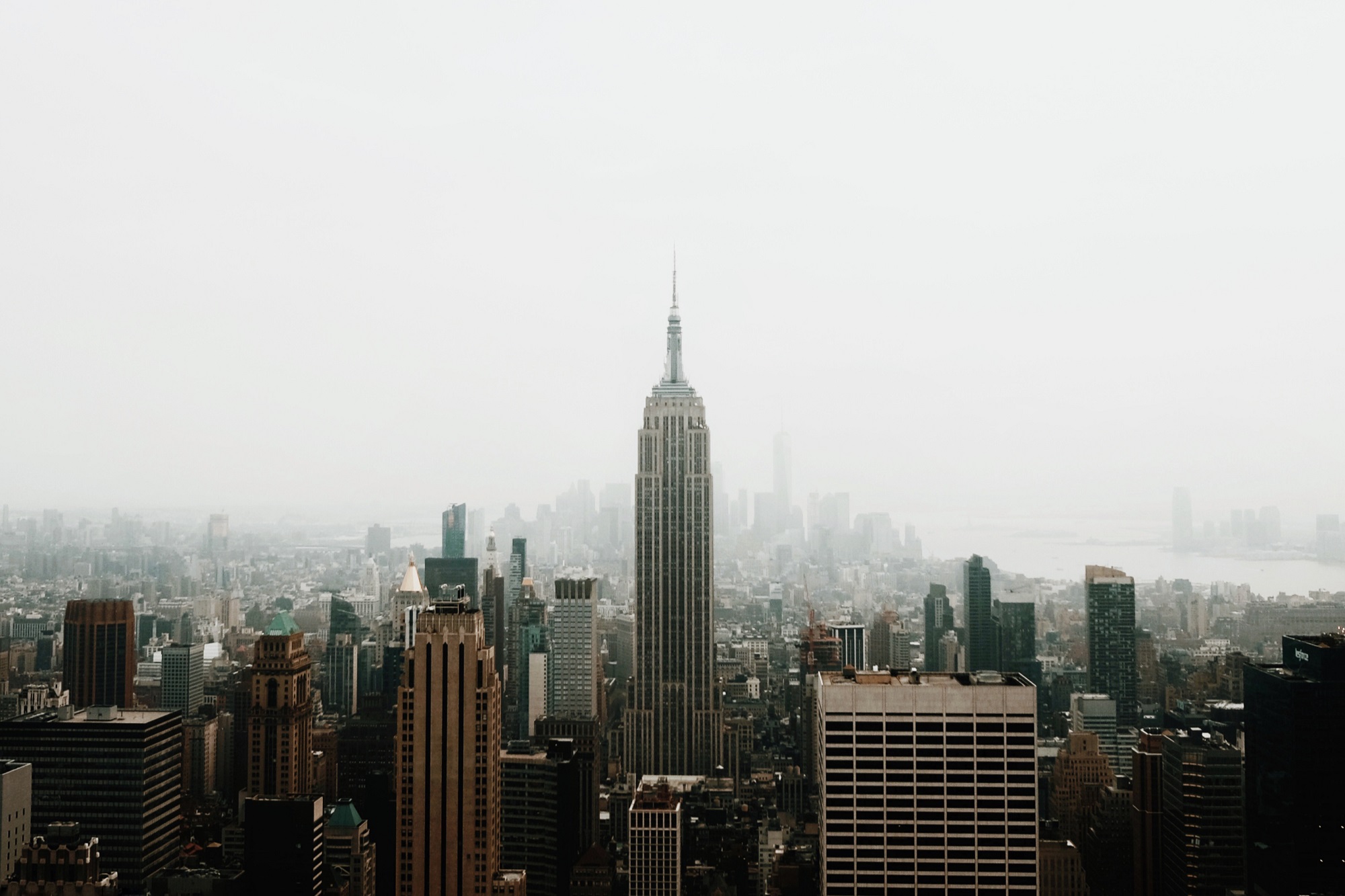Skyline view of New York City featuring the Empire State Building amidst tall buildings under a cloudy sky.