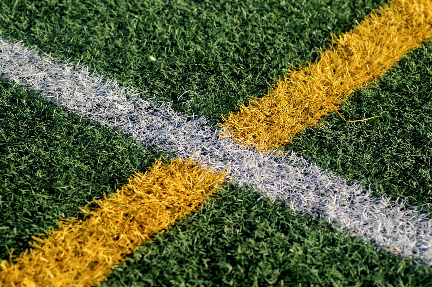 Green artificial turf with white and yellow field lines intersecting.