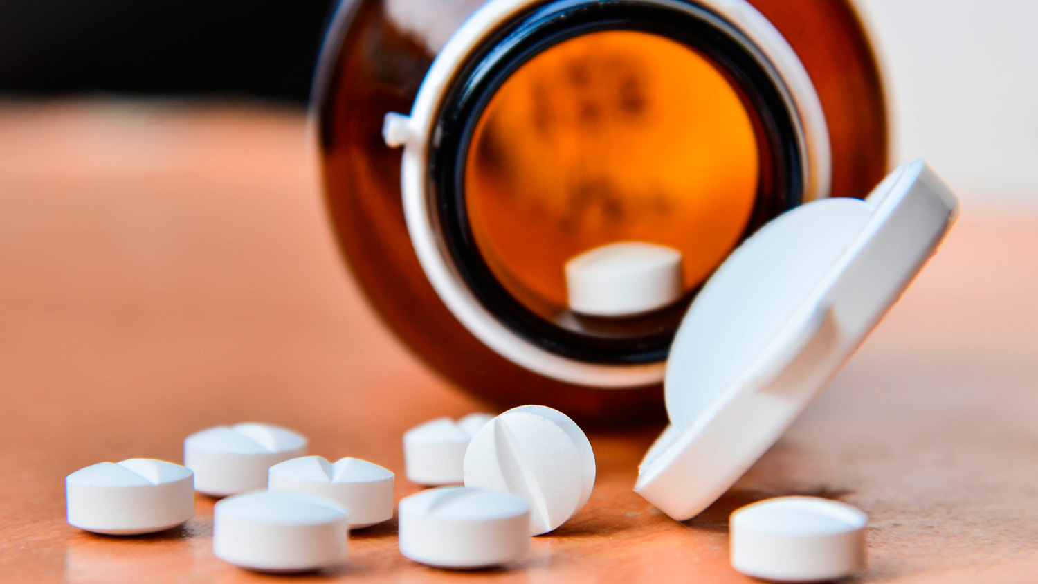 Brown pill bottle tilted with white tablets scattered on a surface.