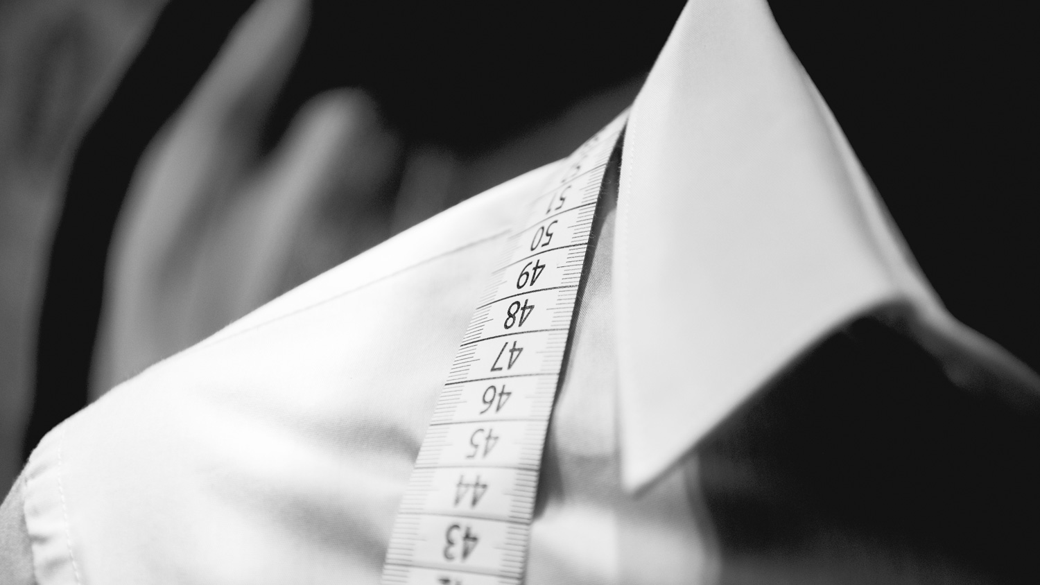 Measuring tape placed on a white collar shirt, indicating tailoring or fitting for formal attire.
