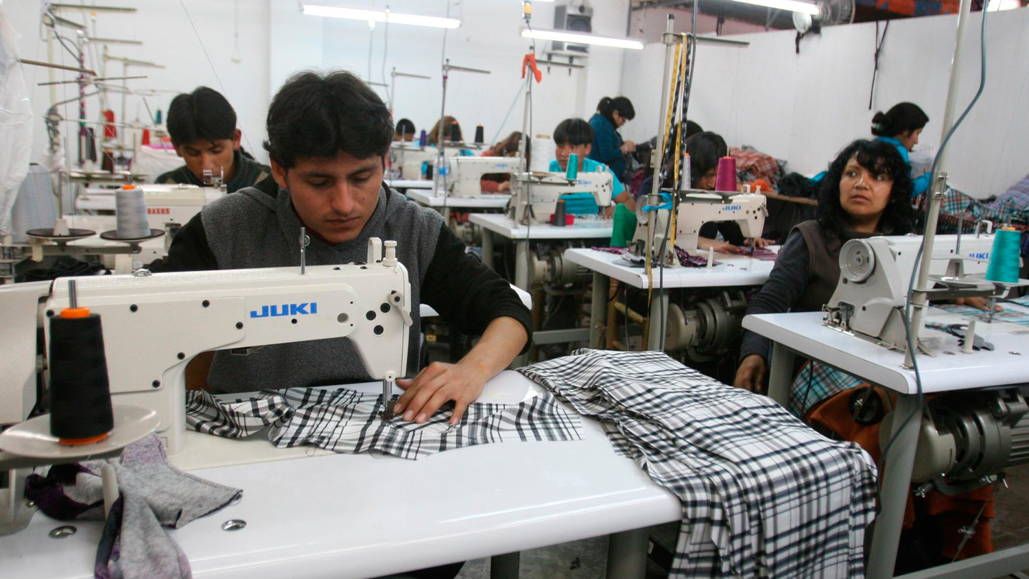 Workers operating sewing machines in a textile workshop, focused on garment production and fabric handling.