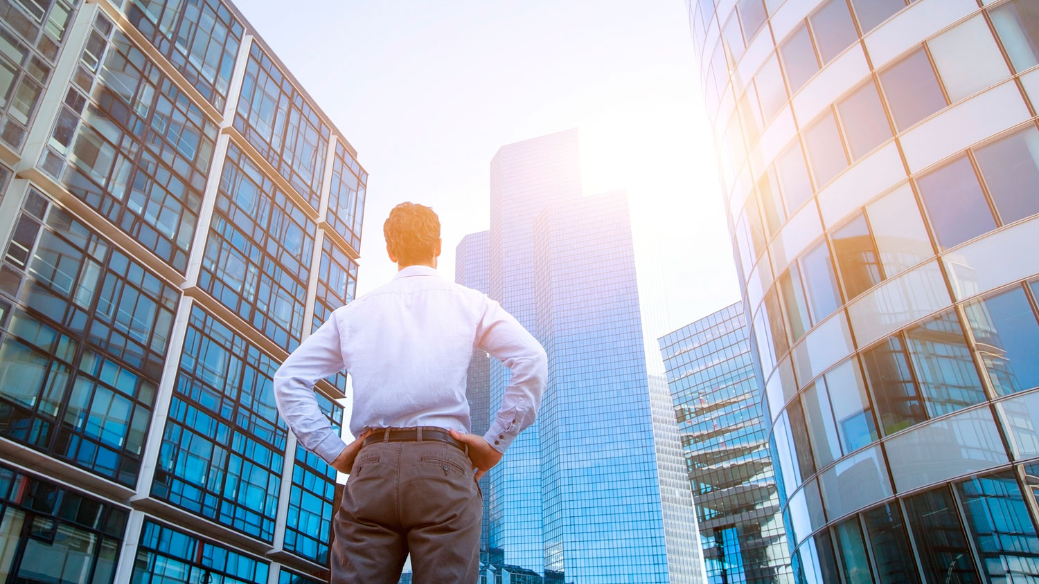 Professional in business attire observing modern office buildings in an urban setting.