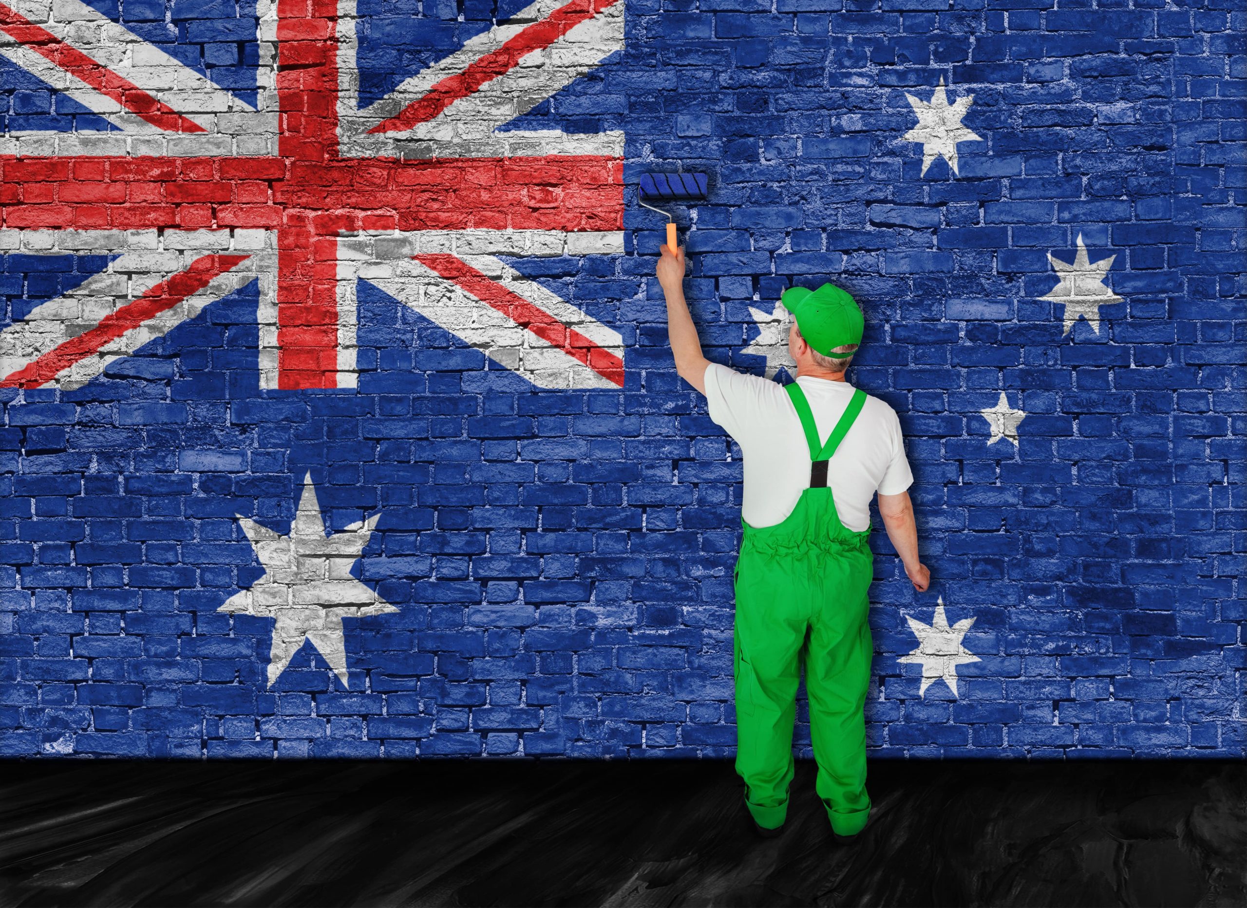 Person painting the Australian flag on a brick wall, using a paint roller, in a creative setting.