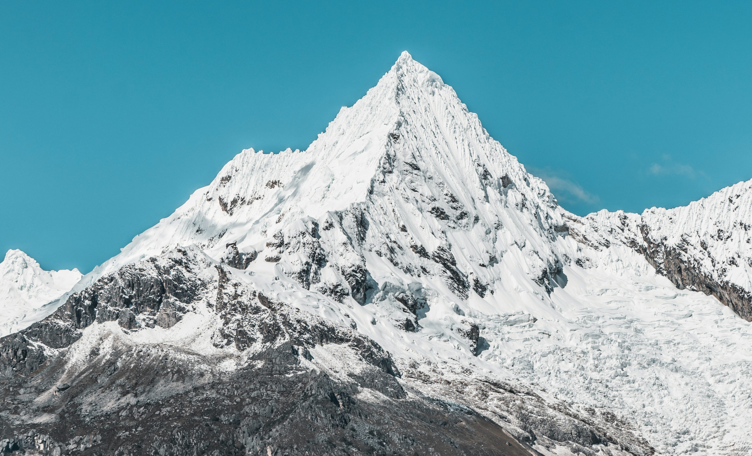 Snow-capped mountain peak against a clear blue sky with rugged terrain below.