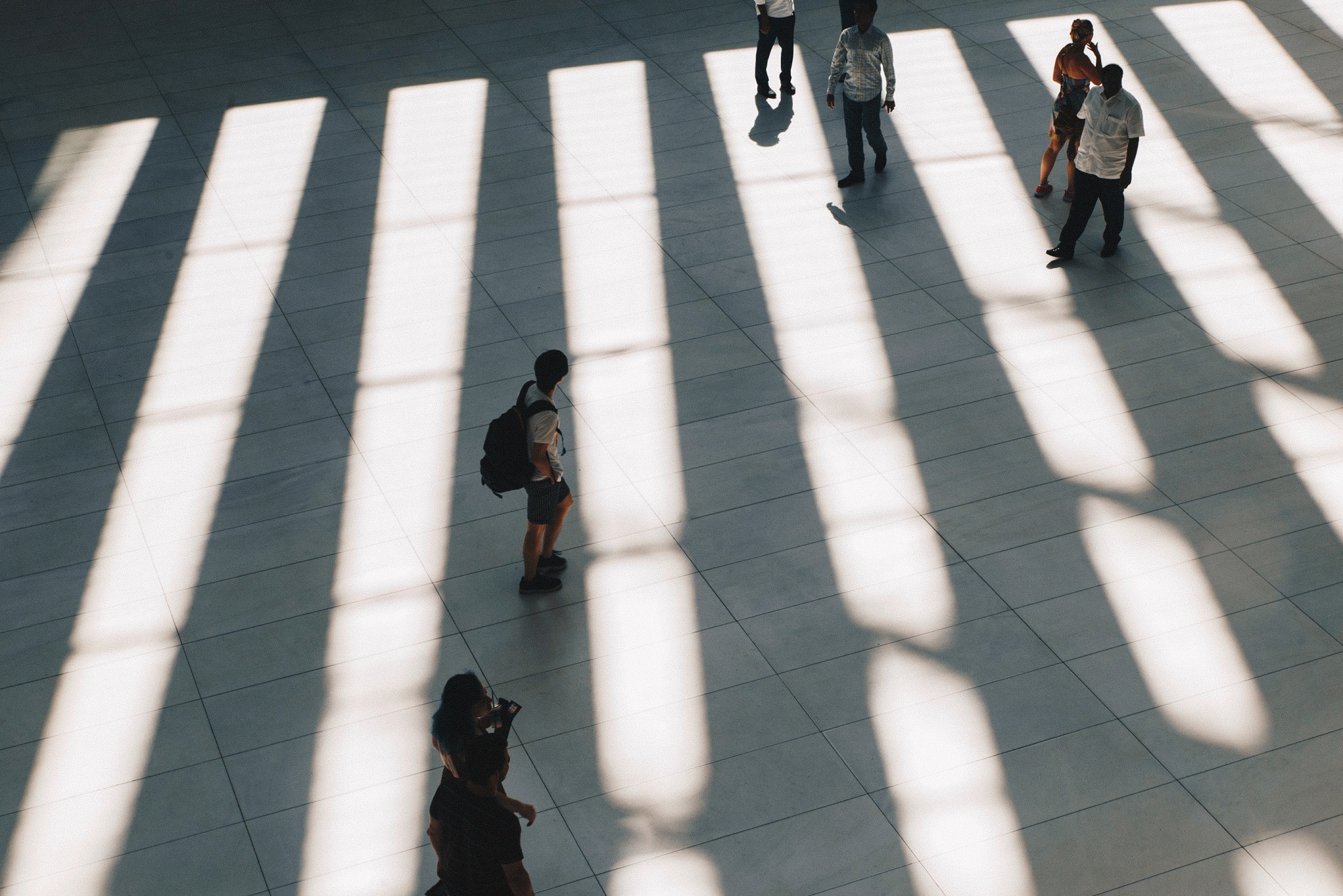 People walking through a spacious area with sunlight casting shadows on the floor.