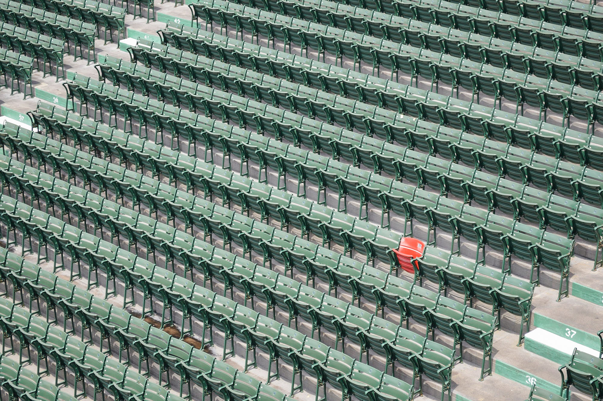 Empty stadium seating with rows of green chairs and a single red chair prominently displayed in the center.