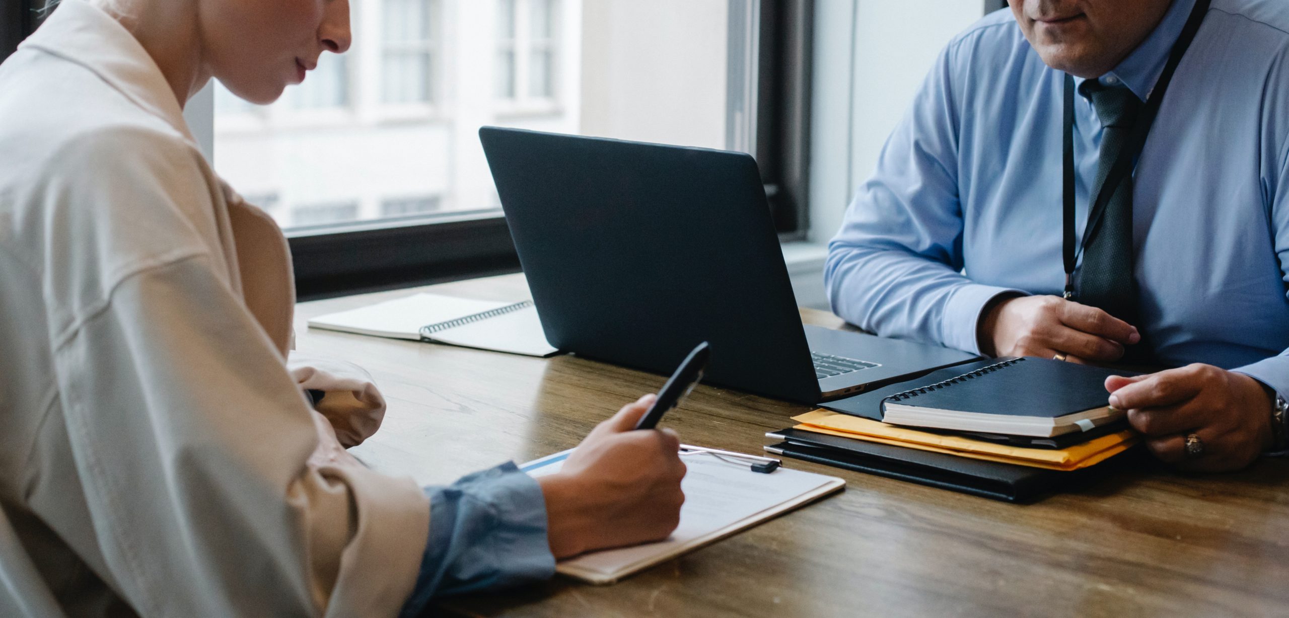 Lawyer consulting with a client while reviewing notes at a desk with a laptop and legal documents.