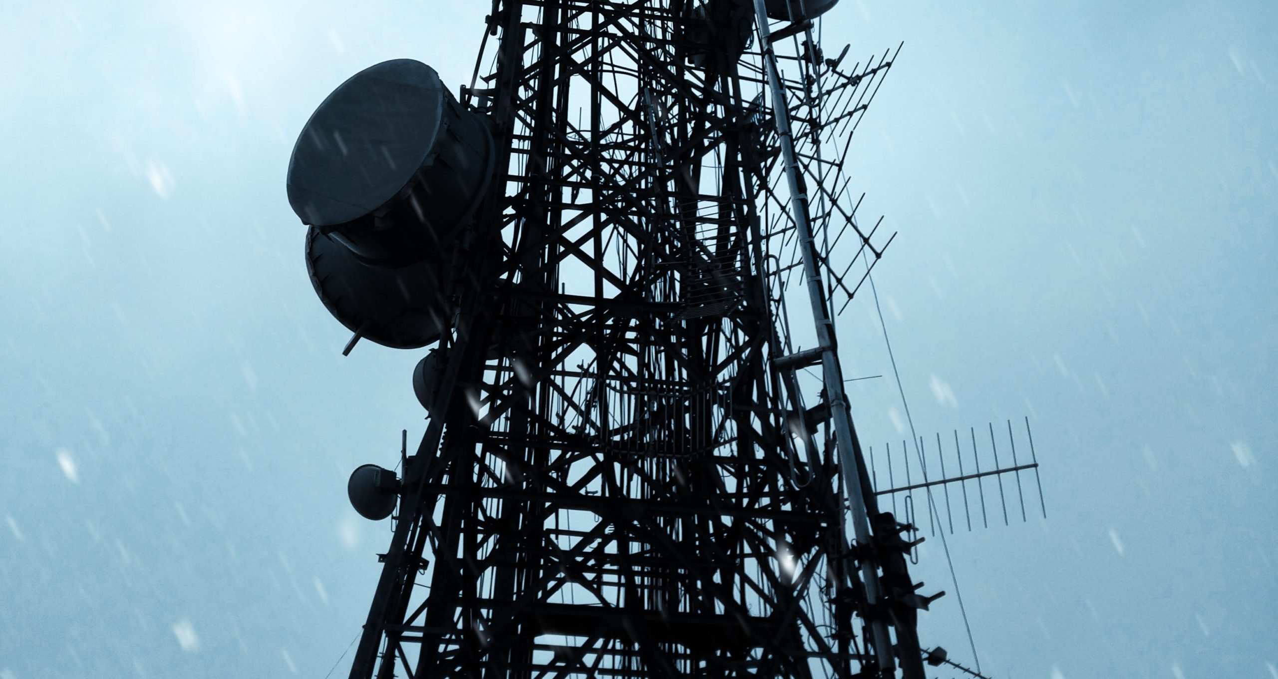 Metallic telecommunications tower with antennas against a cloudy sky.