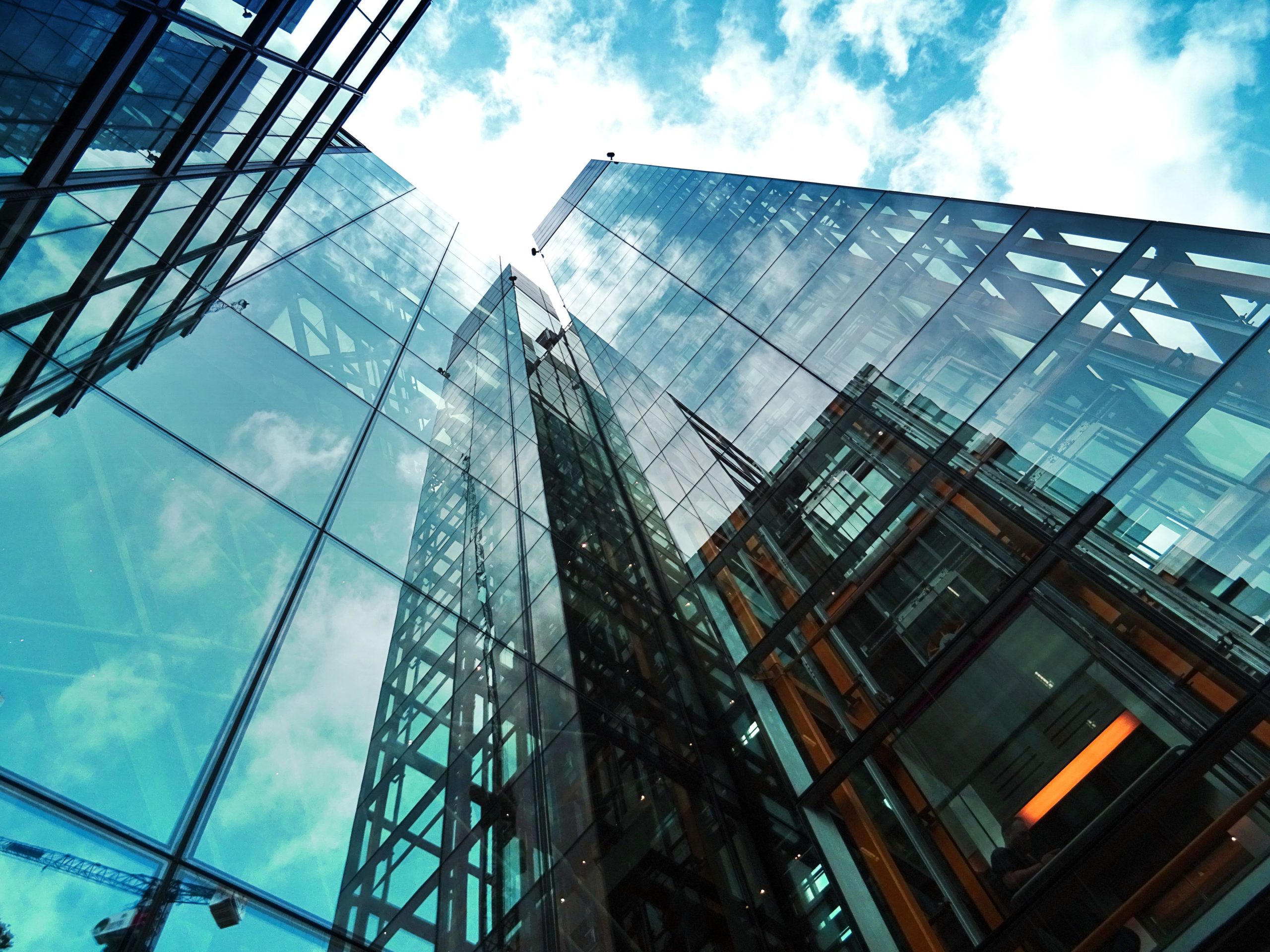 Modern glass office building reflecting clouds and structural elements from surrounding skyscrapers.