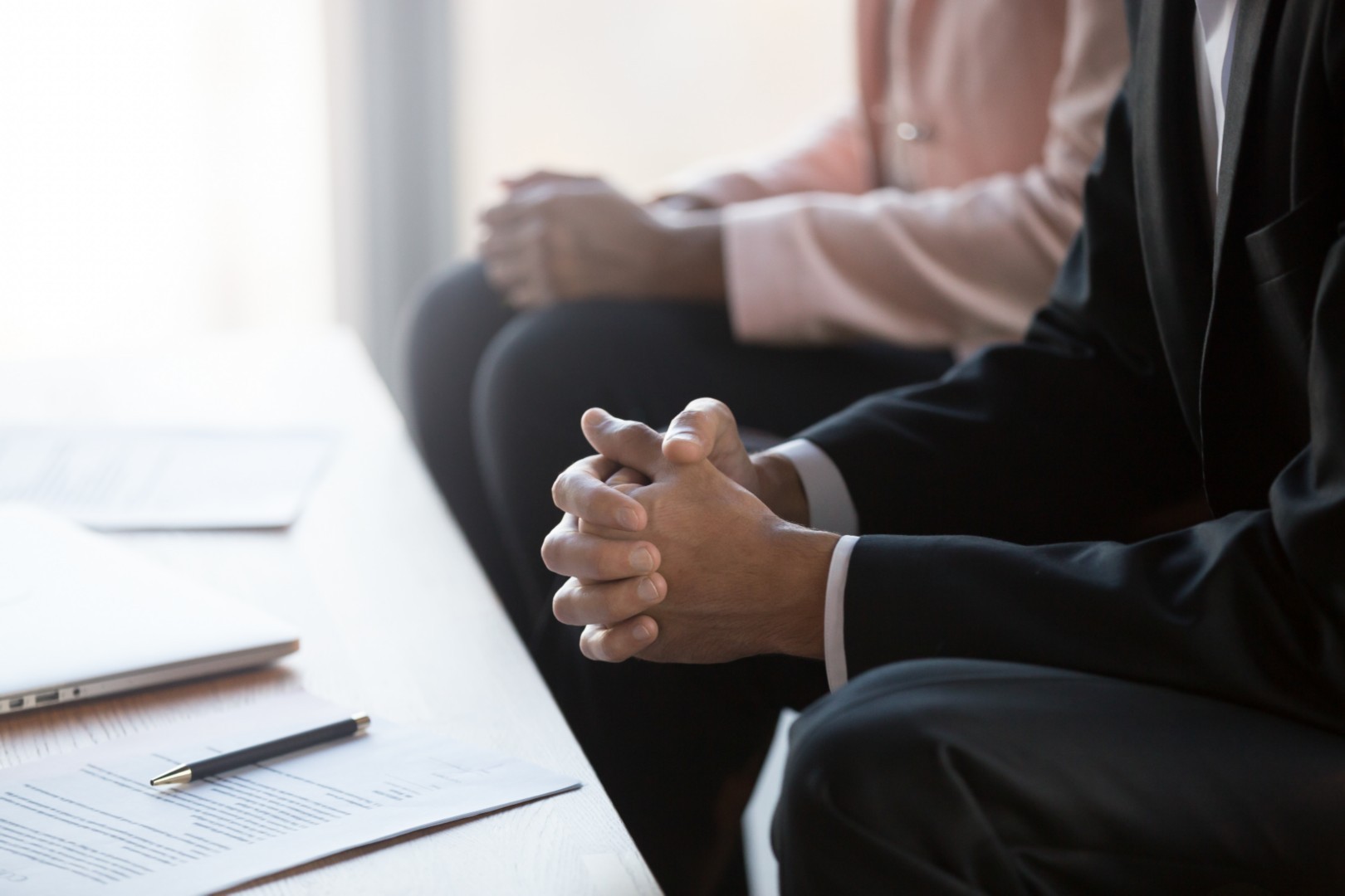 Attorney sitting with hands clasped in a law office during a consultation session, documents visible on the table.