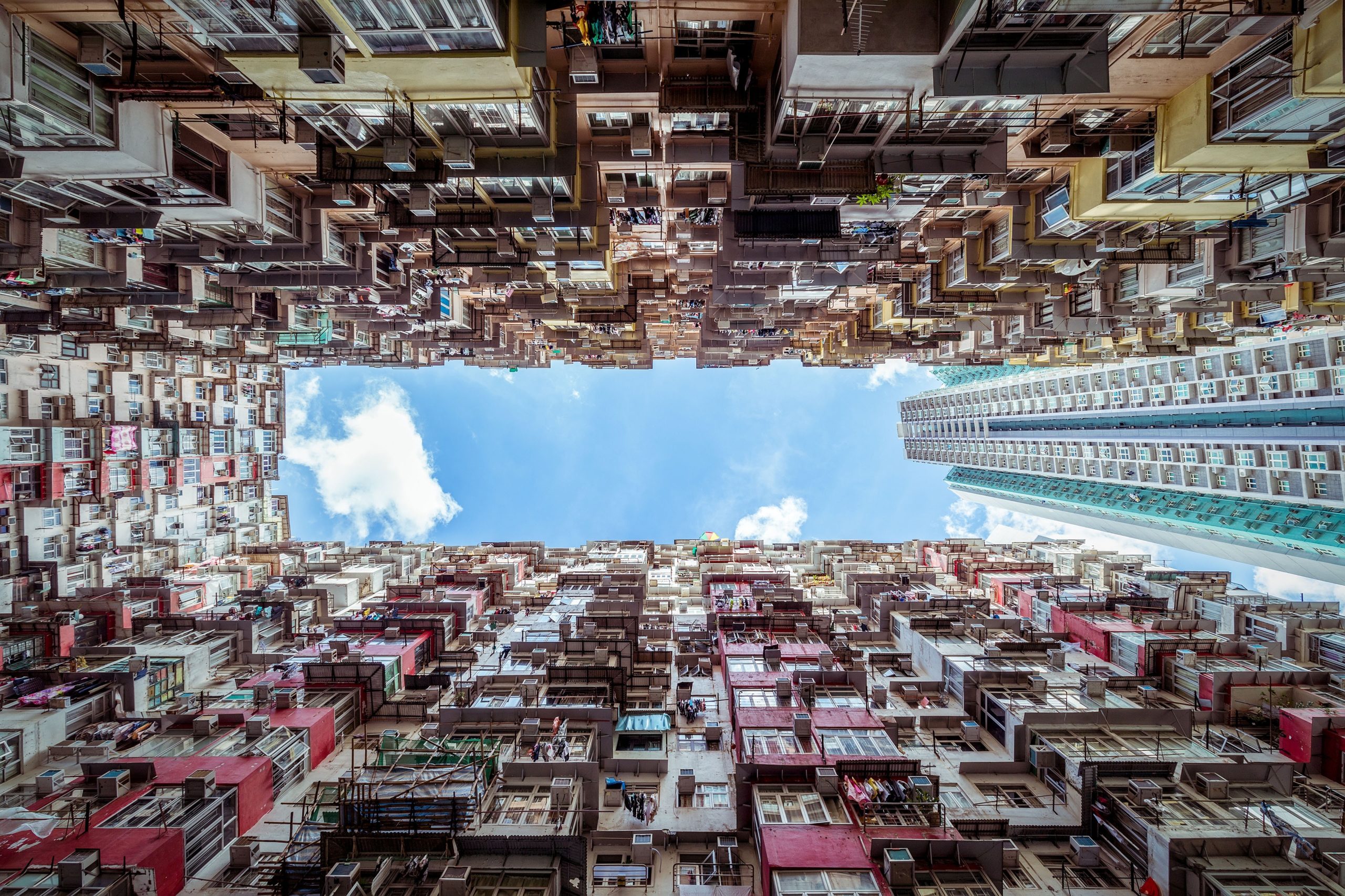 Residential buildings viewed from below, showcasing densely packed apartments against a blue sky.