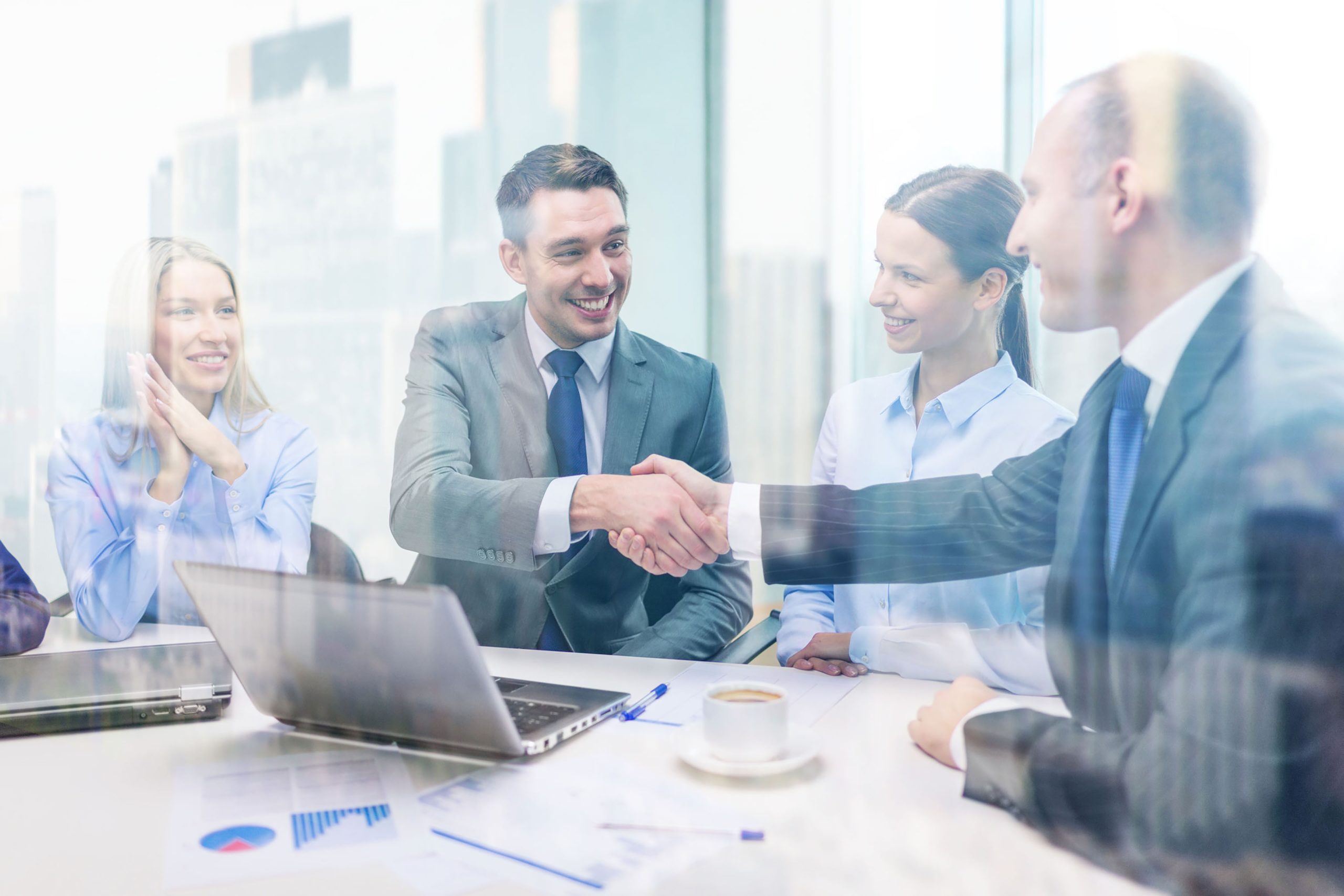 Business professionals shaking hands during a meeting in a modern office with laptops and documents on the table.