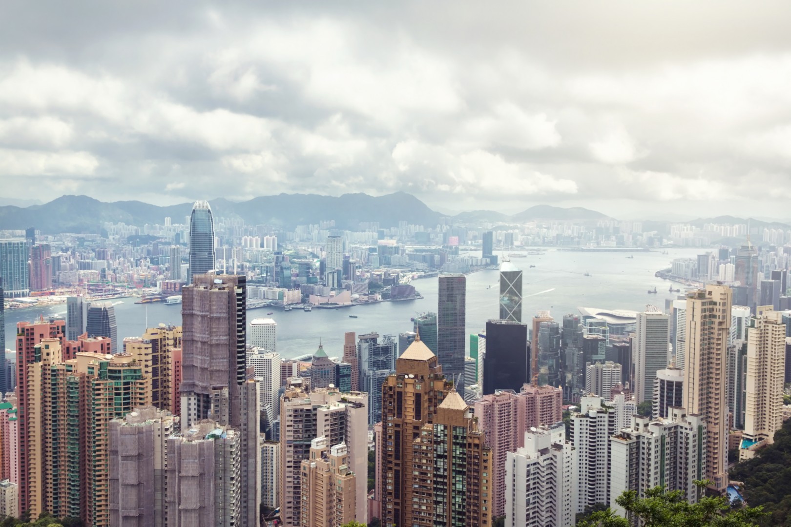 City skyline featuring modern skyscrapers and a waterfront with boats, set against a cloudy sky.