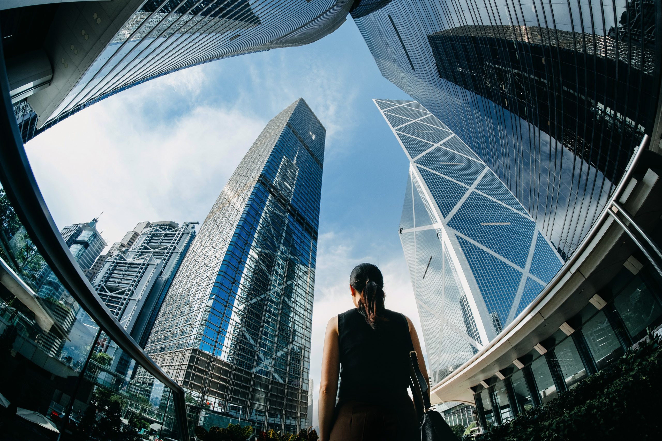 Person standing at the base of tall modern skyscrapers, looking up at the architectural designs.