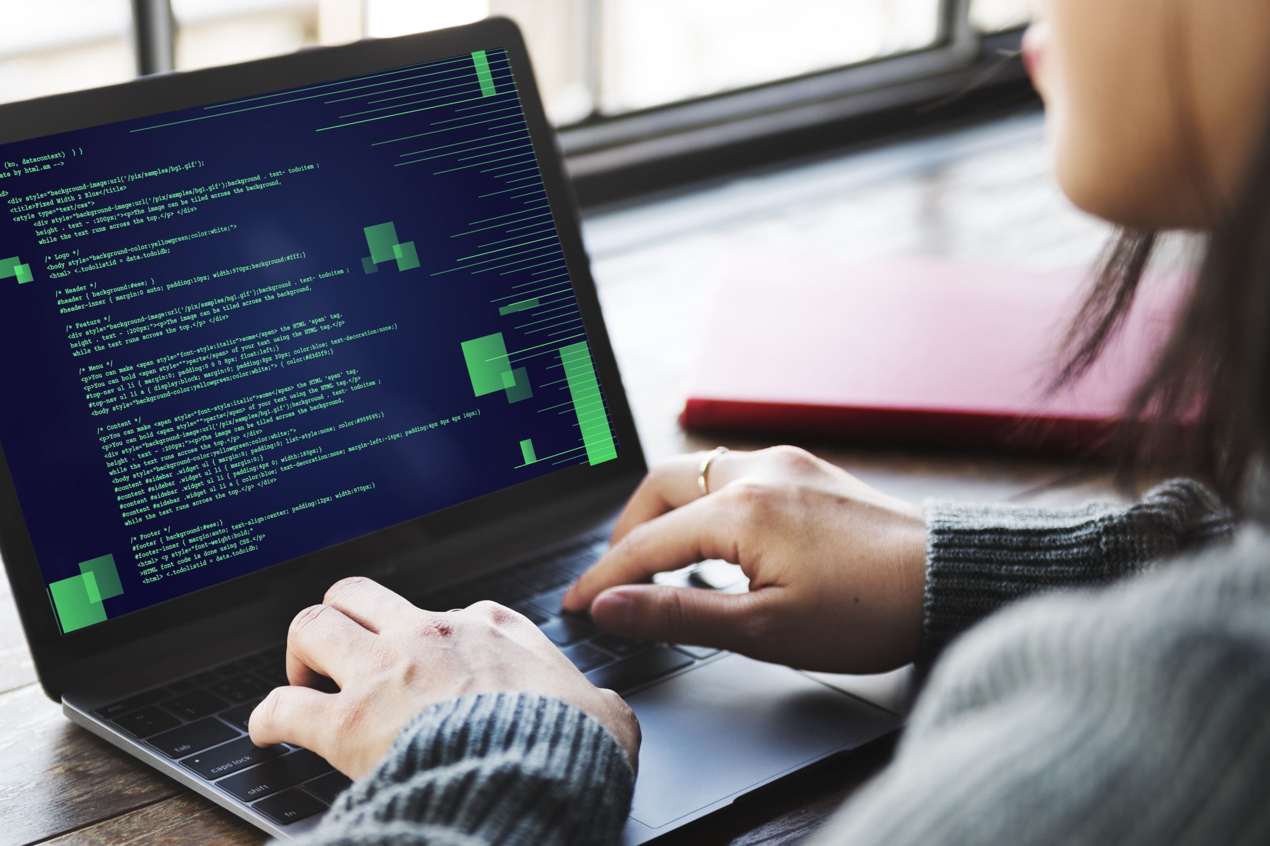 Person typing on a laptop displaying coding text in a casual workspace environment.