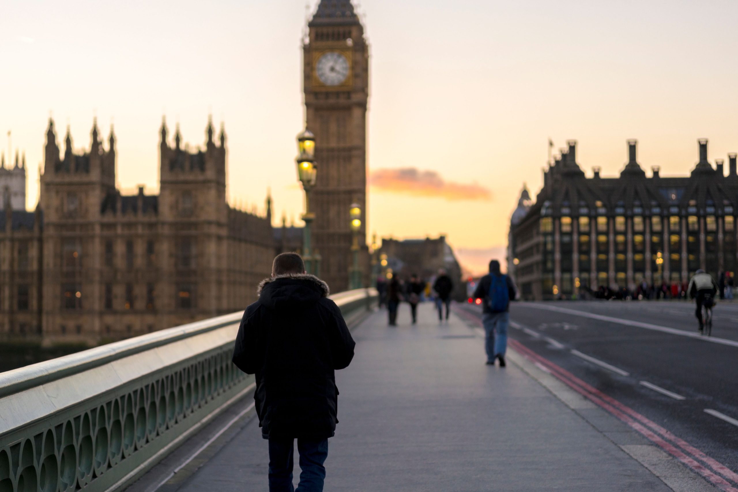 Person walking on bridge with Big Ben and the Houses of Parliament in the background during sunset.