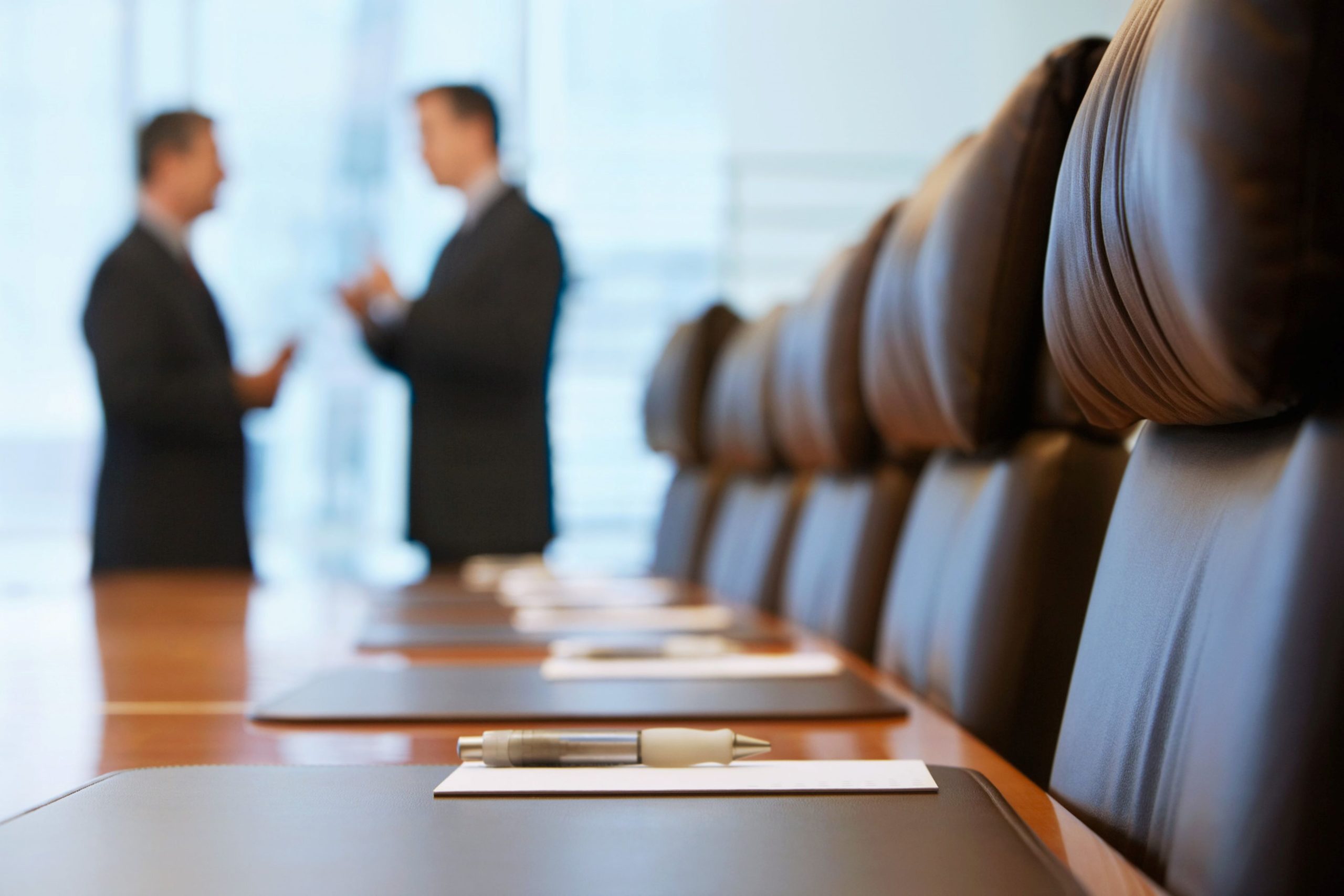 Two lawyers engaged in discussion in a modern conference room with wooden table and leather chairs.