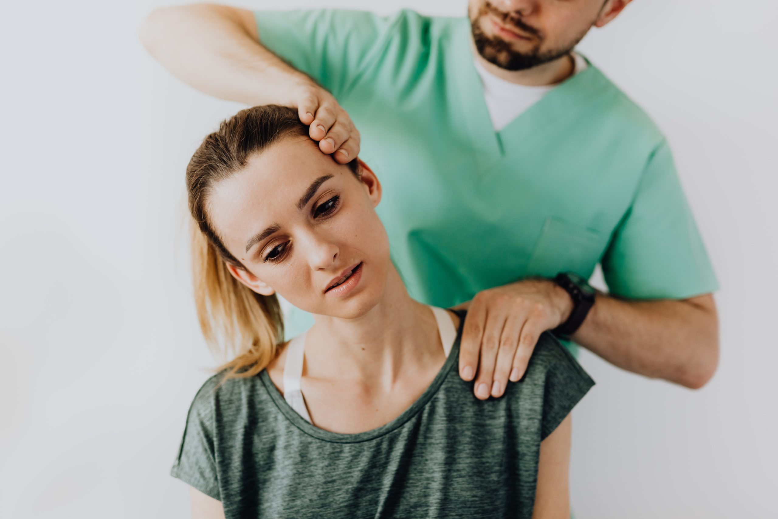 Male professional adjusting the neck of a seated woman in a clinical setting.