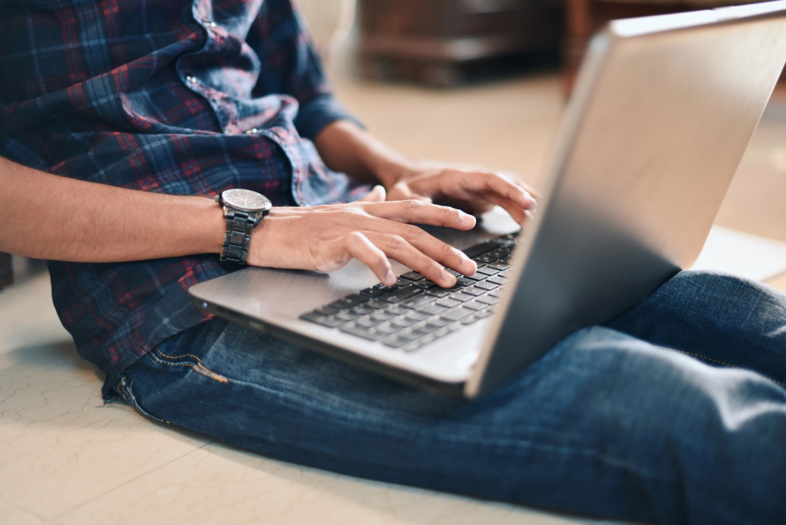 Person typing on a laptop while seated on the floor, in a casual indoor setting.