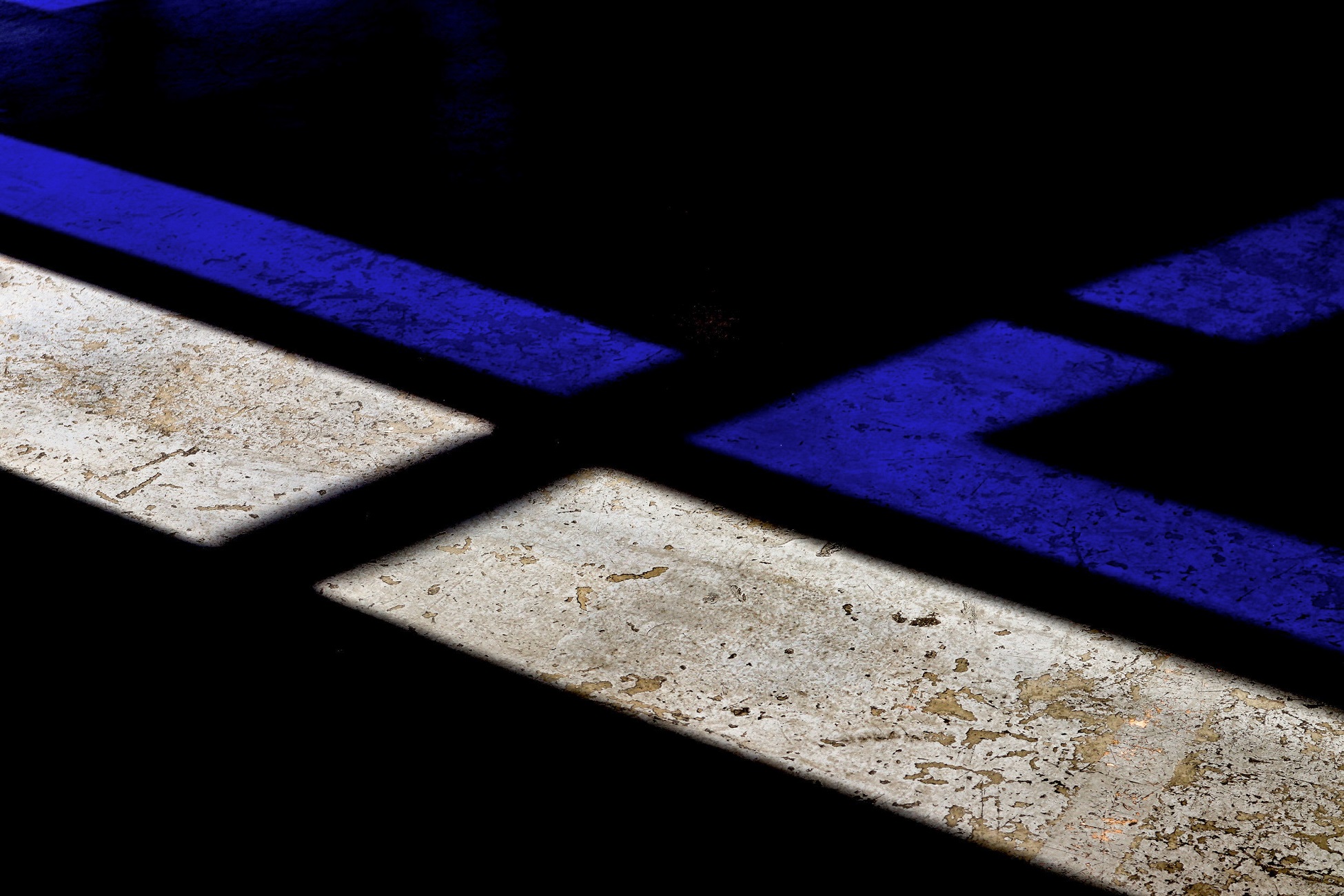 Geometric patterns of light and shadow on a concrete surface with blue and white stripes.