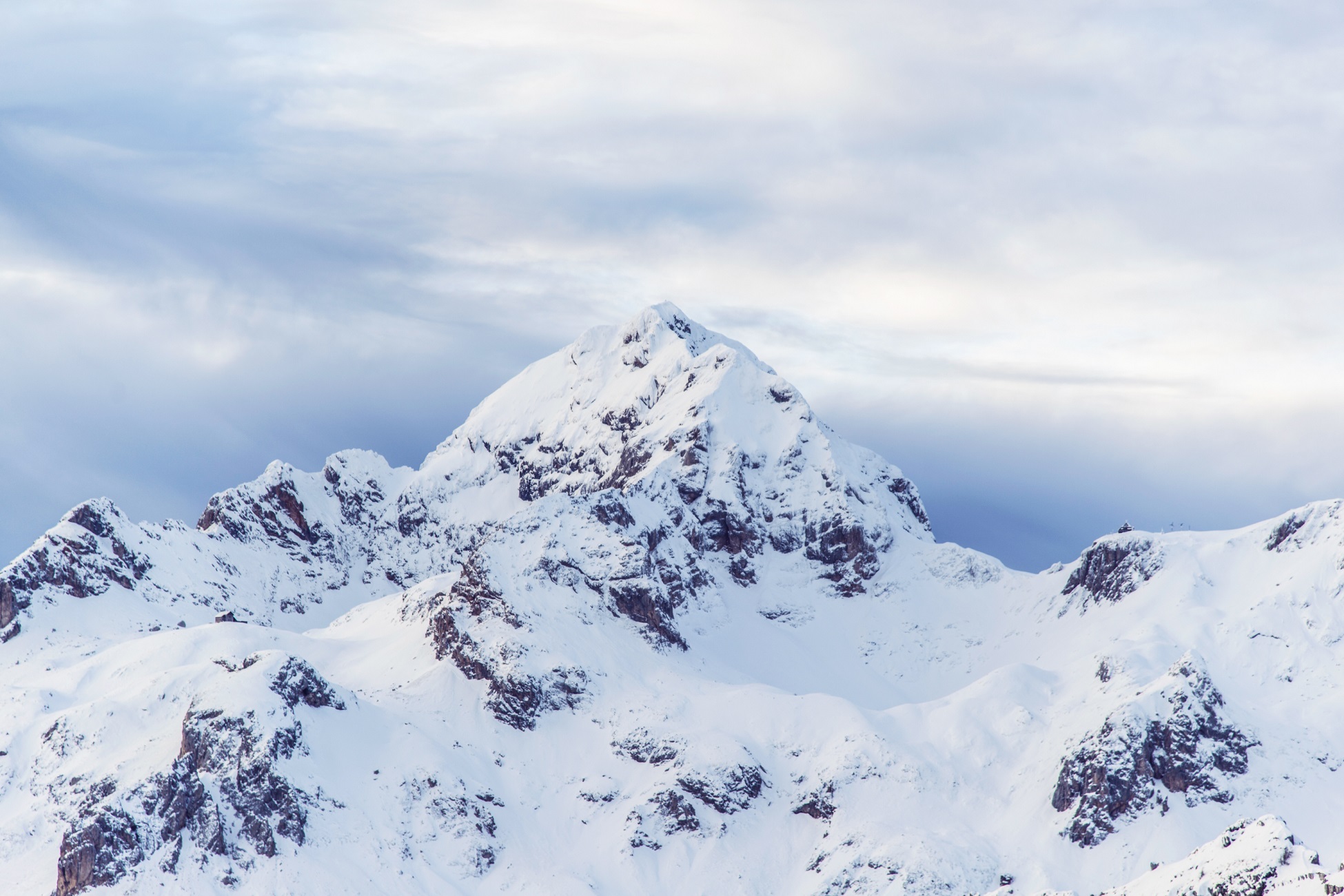 Snow-covered mountain peak under a cloudy sky, showcasing rugged terrain and natural beauty.