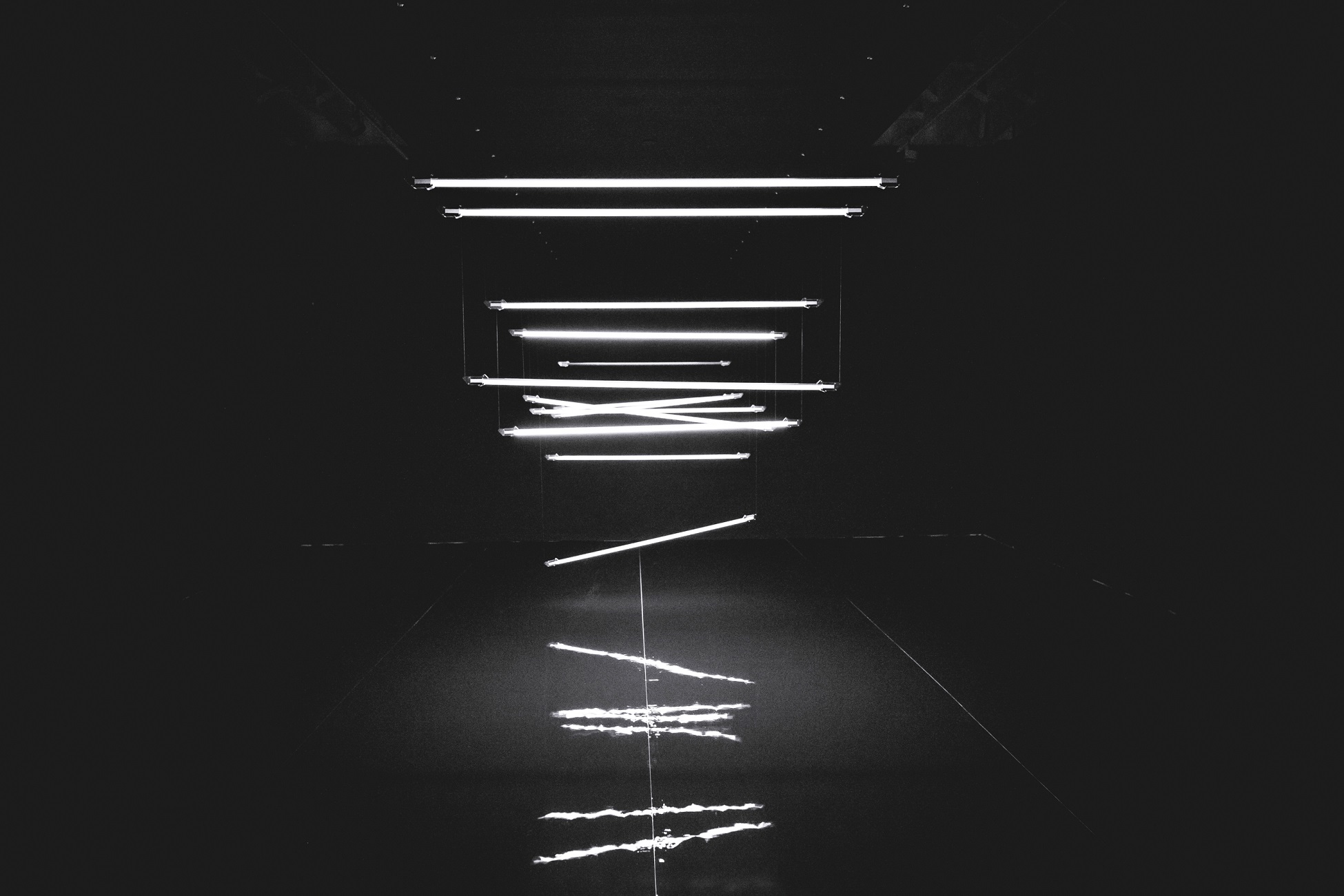 Installation of illuminated lines creating geometric patterns in a dark space.