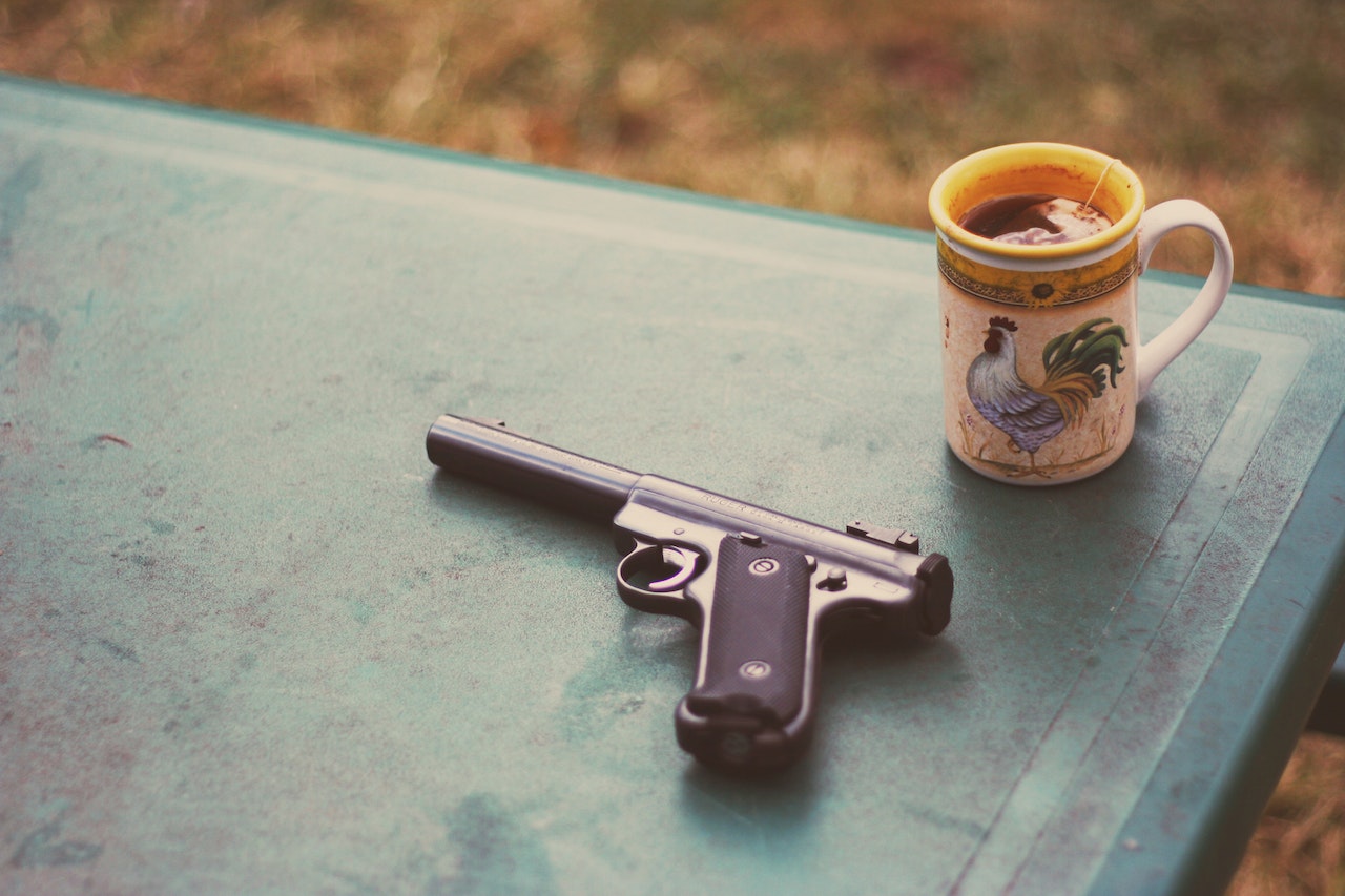 Black pistol resting on a green table beside a decorative coffee mug.