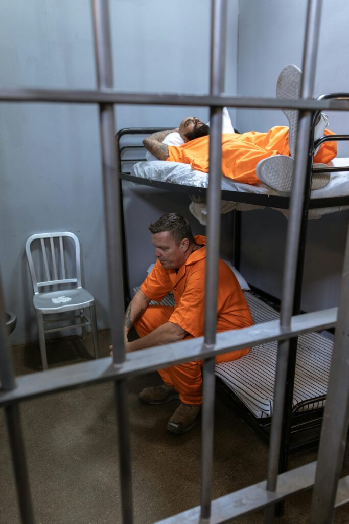 a man sitting on a bunk bed next to another man Prison-Expansion-Crisis Global-Law-Expert