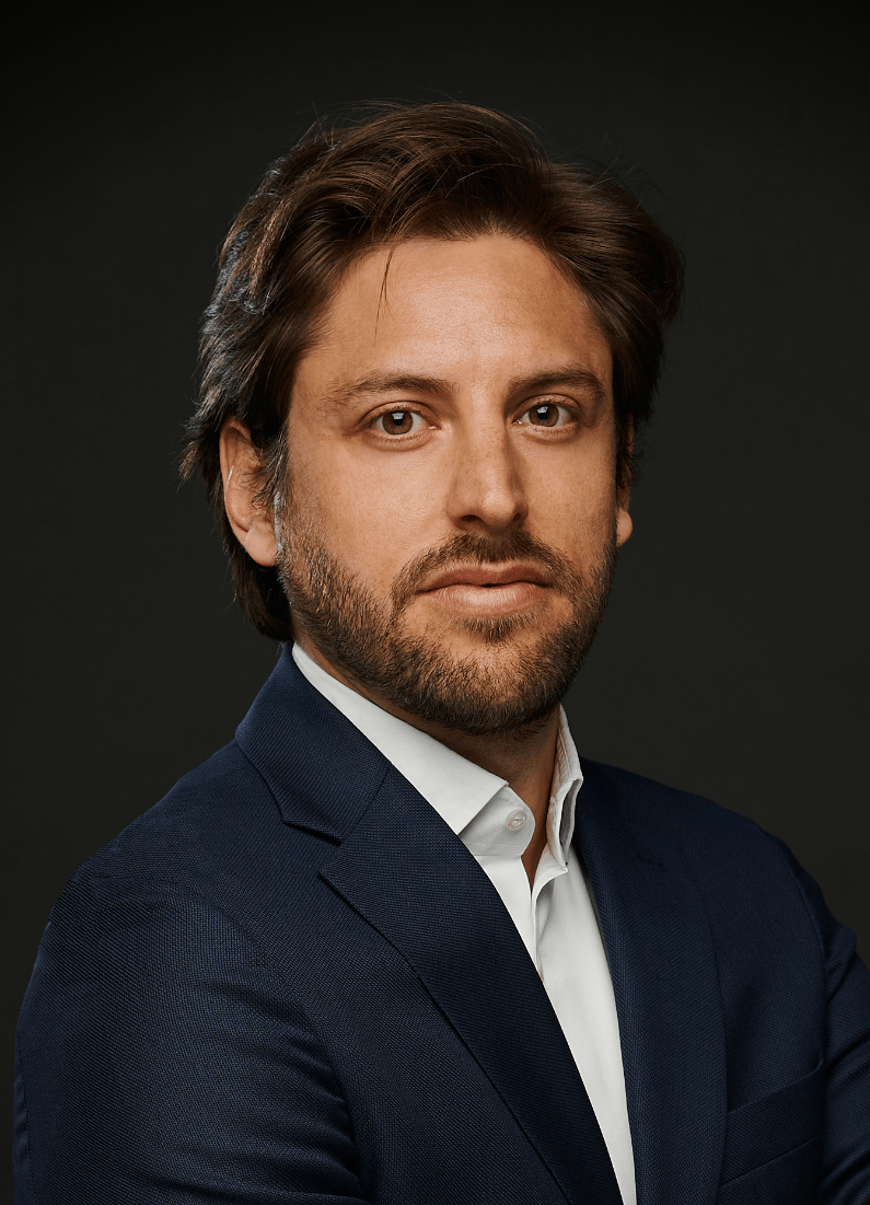 Lawyer in a dark suit, looking directly at the camera, against a plain dark background.