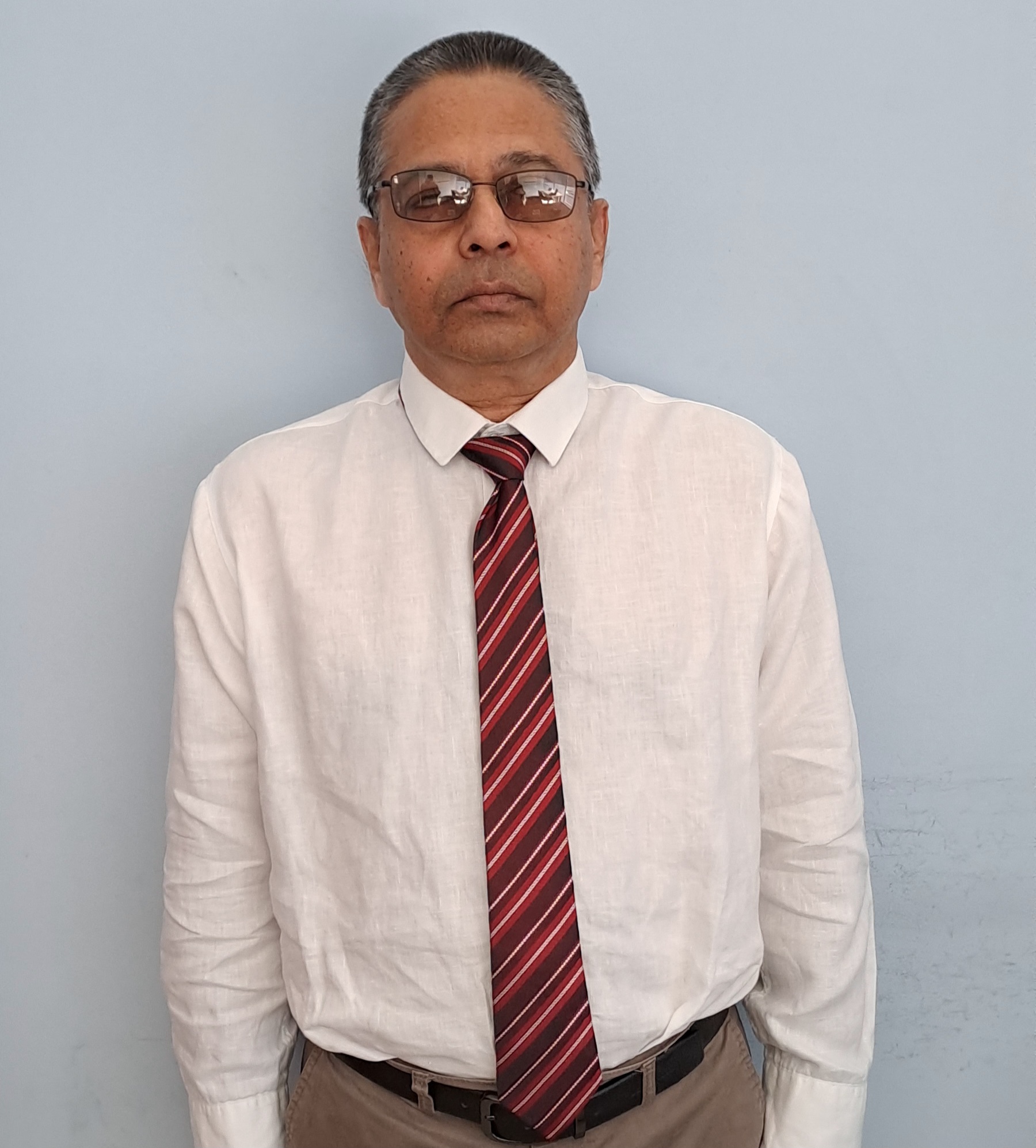 Legal professional in formal attire standing against a light wall, wearing glasses and a striped tie.