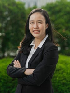 Legal Professional Smiling With Arms Crossed Against A Green Background In A Formal Business Suit.