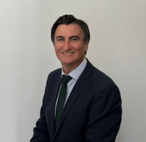 Professional Attorney In A Suit Smiling While Seated Against A Neutral Background.