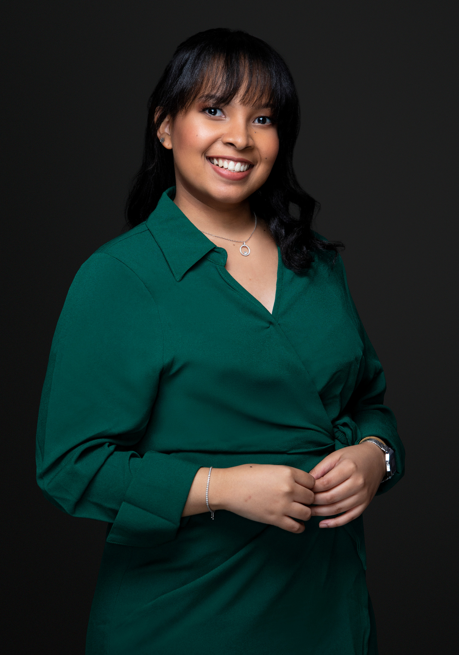 Professional Smiling Woman In A Green Blouse, Posed For A Portrait Against A Dark Background.