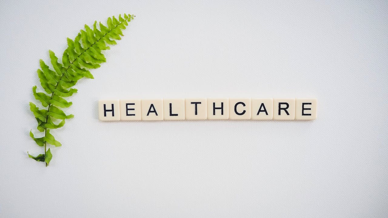 Scrabble tiles spelling "HEALTHCARE" with a green fern placed alongside them on a white background.