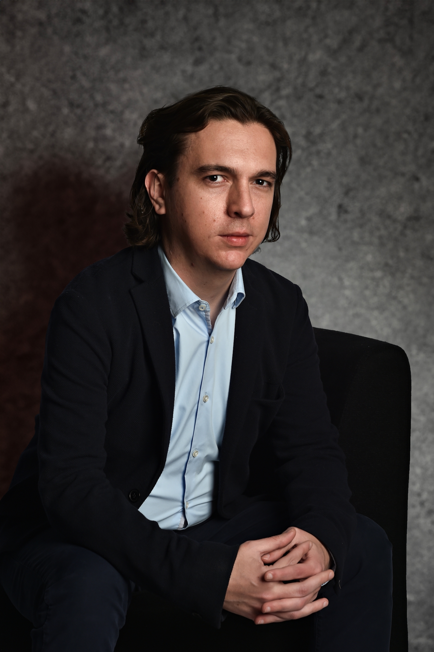Attorney sitting in a chair, engaged in a thoughtful expression against a neutral backdrop.