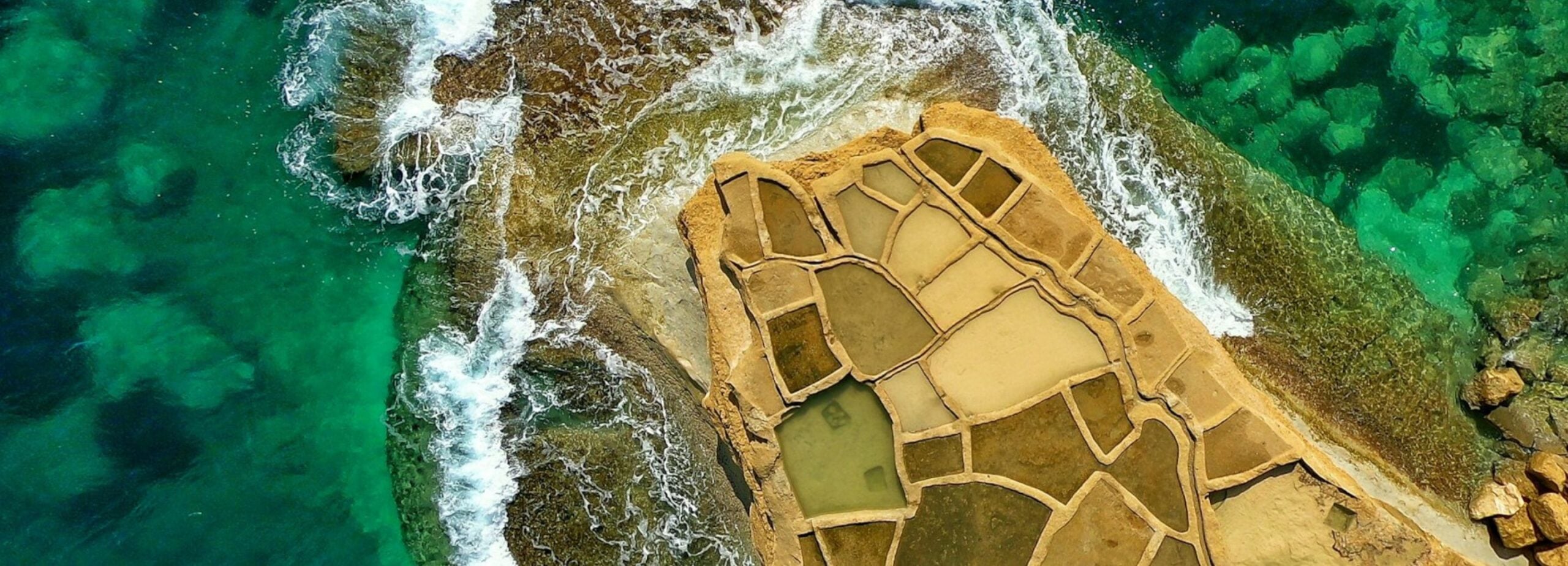 Aerial view of rocky coastline with tidal pools and clear turquoise waters.
