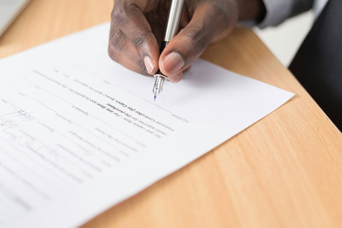 Attorney signing a legal document with a fountain pen on a wooden desk.