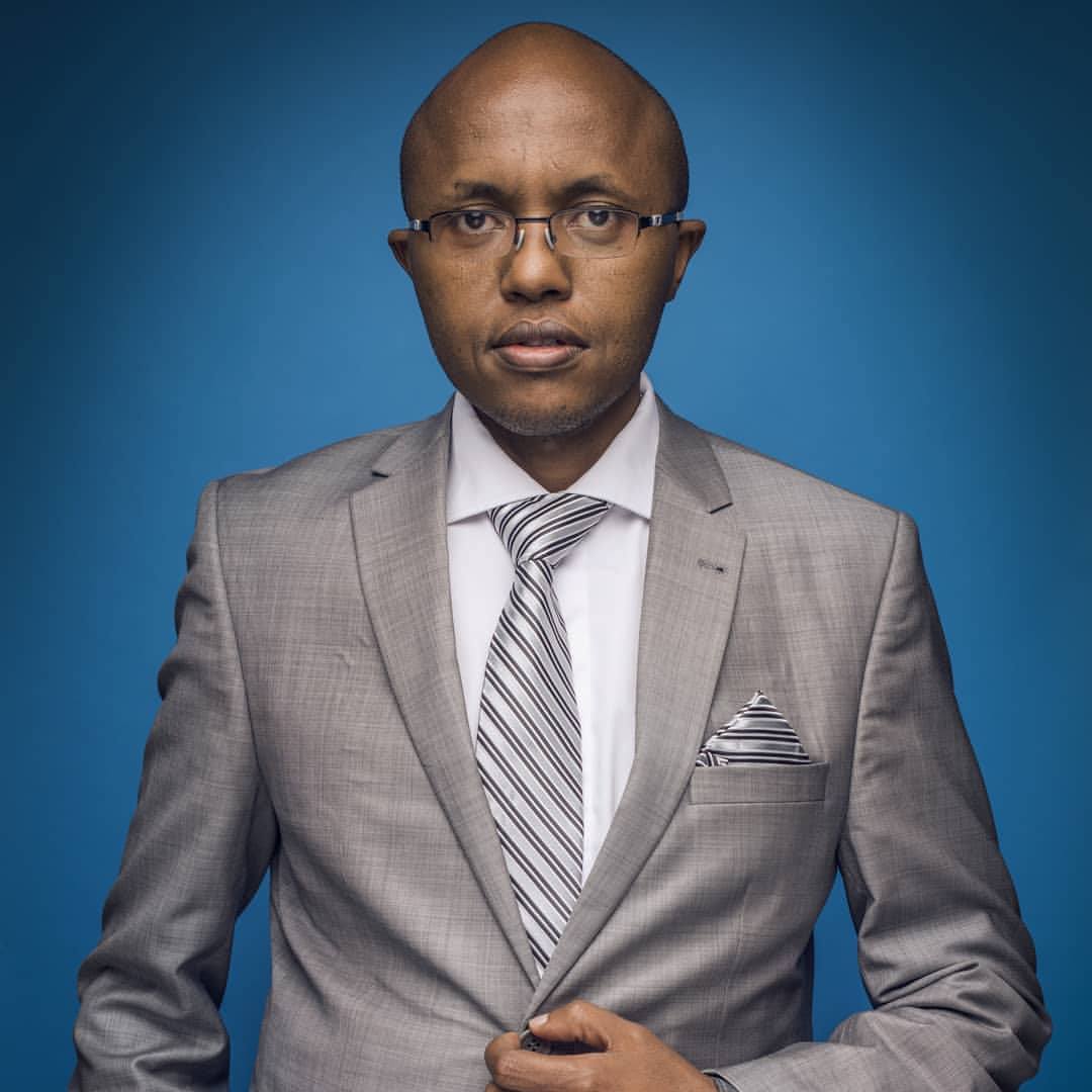 Lawyer in gray suit with striped tie, standing confidently against a blue background.