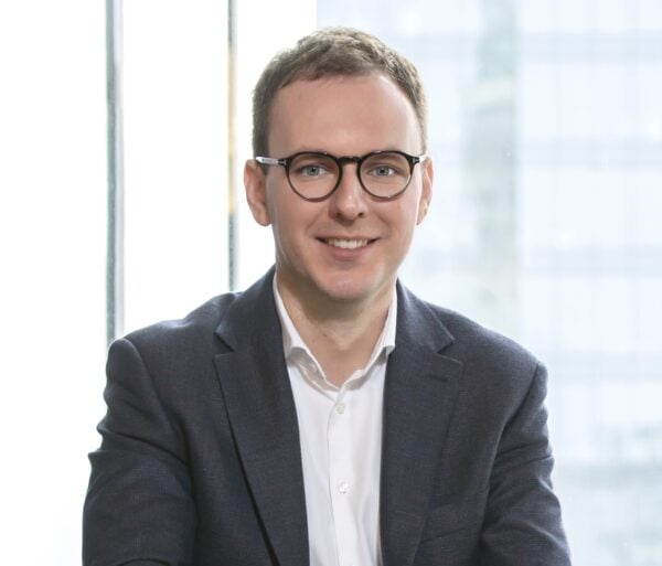 Lawyer smiling and seated in a modern office with large windows and a professional appearance.
