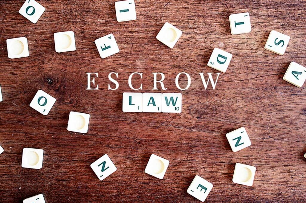 Scrabble tiles arranged on wooden surface spelling "ESCROW LAW" with additional tiles scattered around.