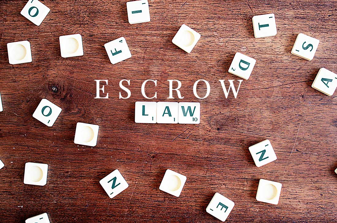 Scrabble tiles arranged on wooden surface spelling "ESCROW LAW" with additional tiles scattered around.