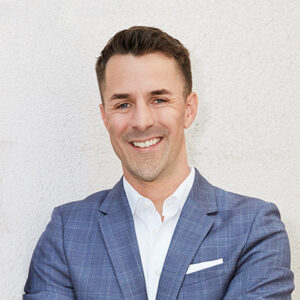 Smiling attorney wearing a blue suit, standing with arms crossed against a neutral background.