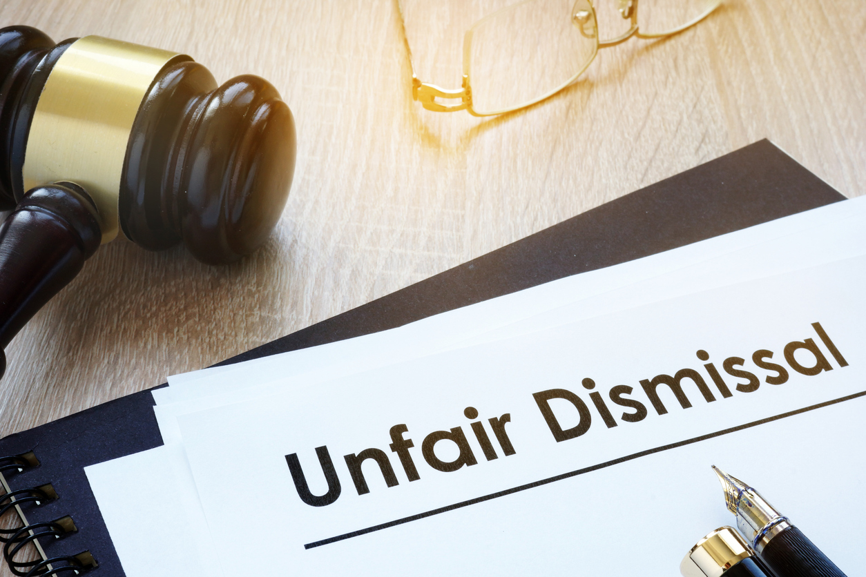 Gavel and documents titled "Unfair Dismissal" placed on a wooden table with a pen and glasses nearby.