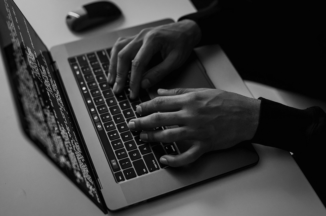 Hands typing on a laptop keyboard displaying code, in a minimalistic office setting.