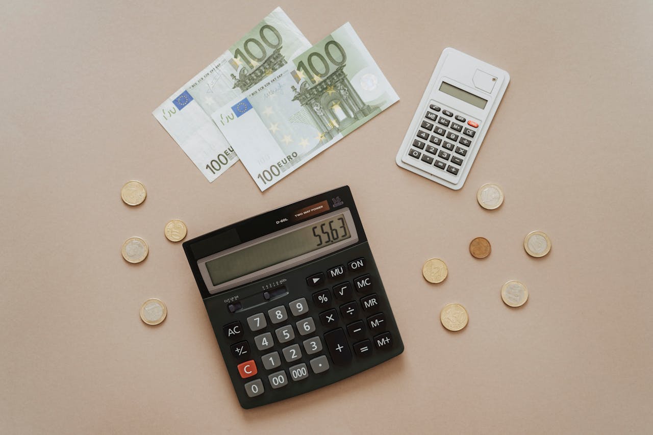 Calculator and Euro banknotes on a neutral background with coins arranged nearby.
