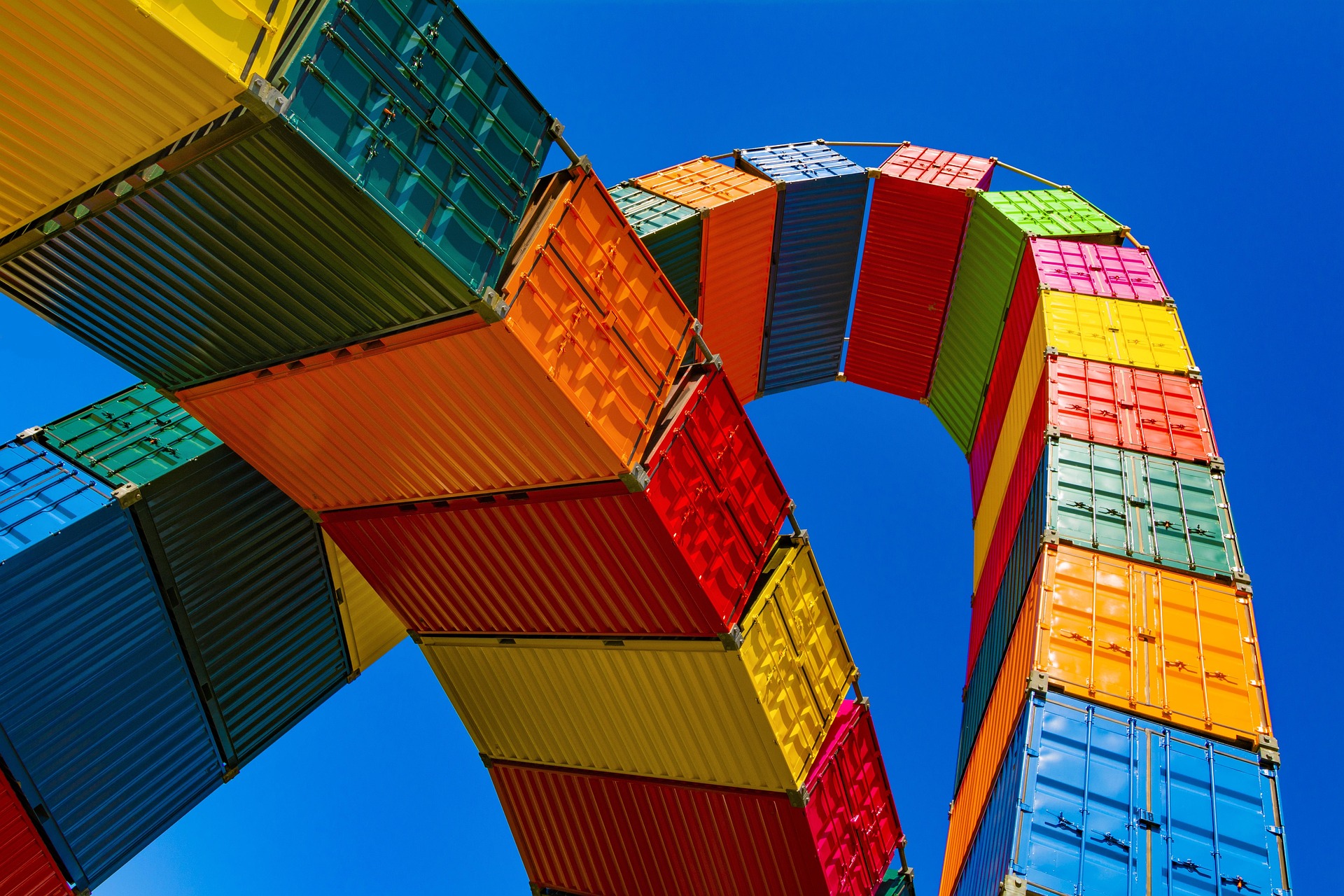 Colorful shipping containers arranged in an arch against a clear blue sky.