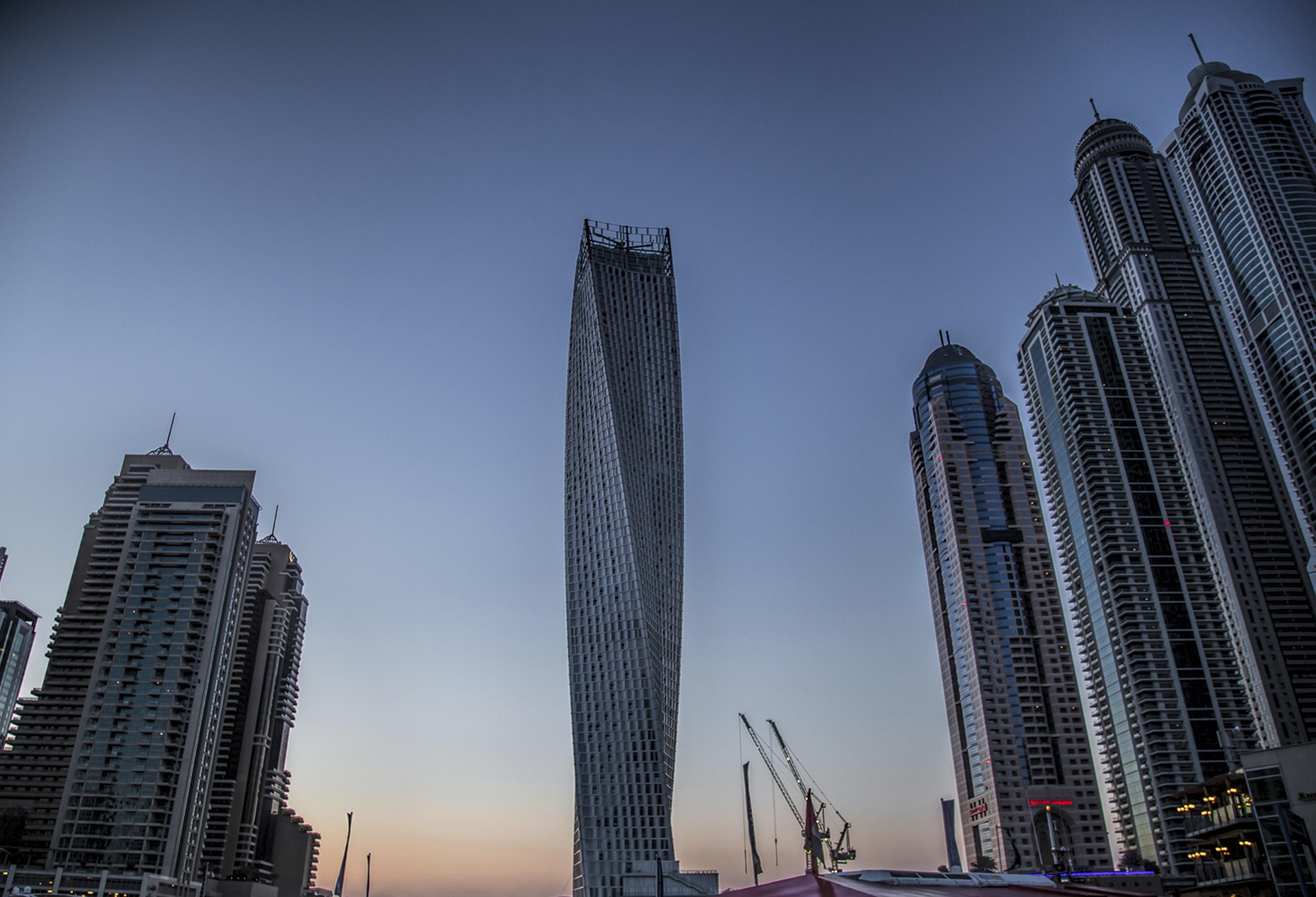 Twisting skyscraper surrounded by modern high-rises against a dusk sky, showcasing a contemporary urban skyline.